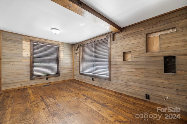 empty room featuring beam ceiling, wood walls, and hardwood / wood-style floors