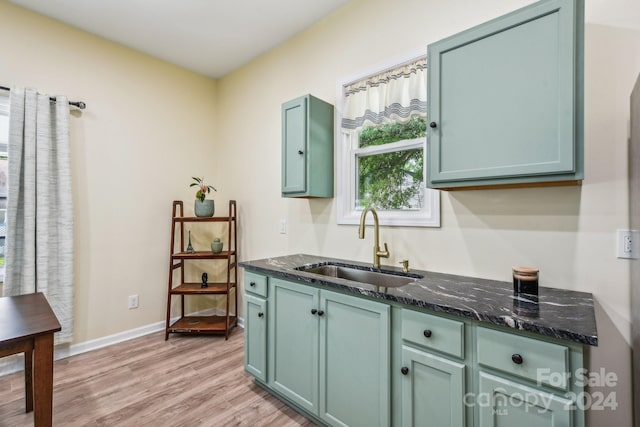 kitchen with sink, green cabinets, light hardwood / wood-style floors, and dark stone counters