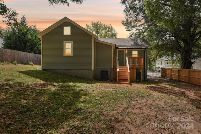 back house at dusk with a yard and central AC unit