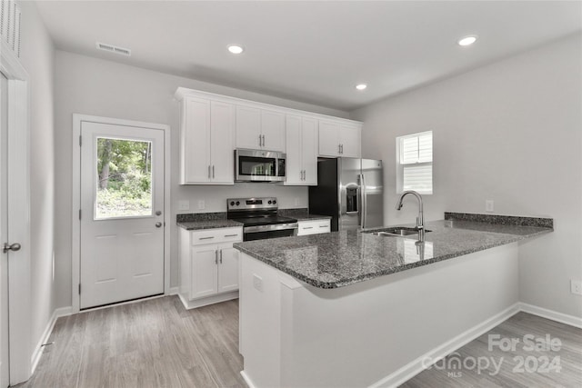 kitchen with stainless steel appliances, kitchen peninsula, a healthy amount of sunlight, and white cabinetry