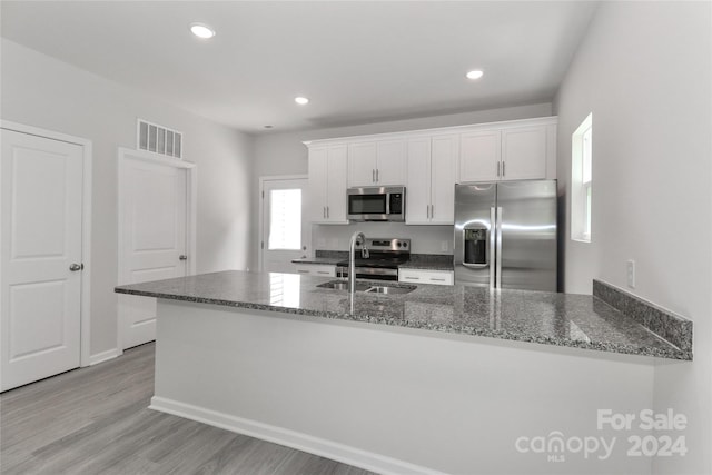 kitchen with dark stone countertops, white cabinets, stainless steel appliances, light wood-type flooring, and sink