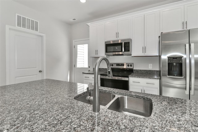 kitchen with white cabinets, stainless steel appliances, sink, and dark stone counters