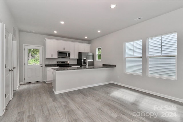 kitchen featuring dark stone countertops, white cabinets, stainless steel appliances, and light hardwood / wood-style floors