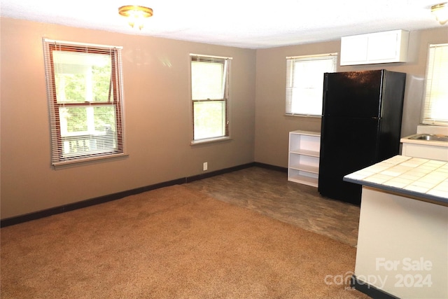 kitchen featuring white cabinetry, tile counters, black fridge, and carpet floors