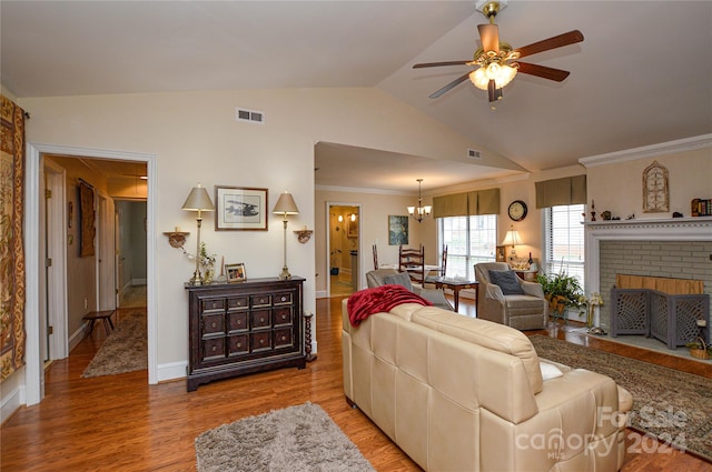 living room with a brick fireplace, ceiling fan with notable chandelier, lofted ceiling, light hardwood / wood-style flooring, and ornamental molding