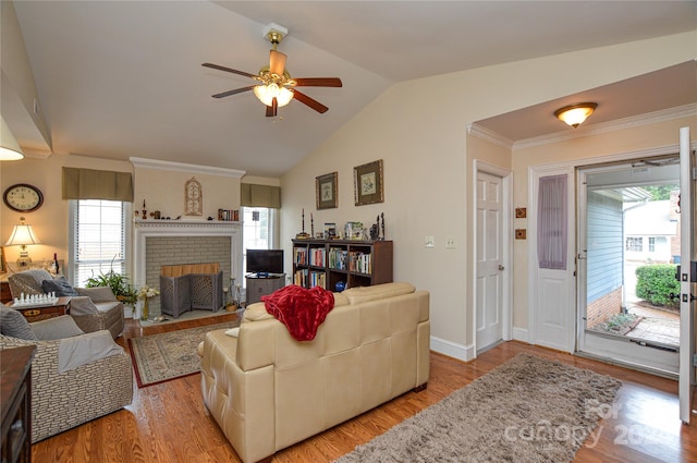 living room featuring ceiling fan, lofted ceiling, ornamental molding, a brick fireplace, and light hardwood / wood-style floors