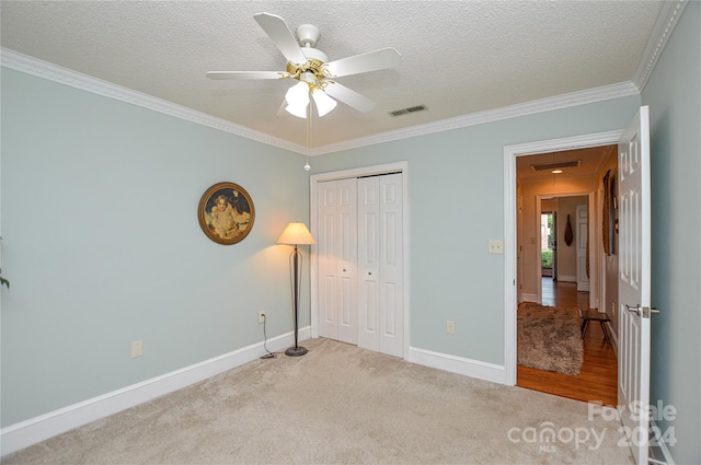 unfurnished bedroom with a closet, a textured ceiling, ceiling fan, ornamental molding, and light colored carpet