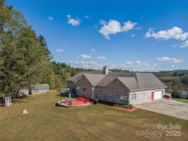 view of front of home featuring a patio, a chimney, a garage, driveway, and a front lawn