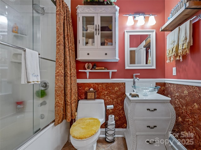 bathroom featuring a wainscoted wall, shower / bath combination with glass door, toilet, and wallpapered walls