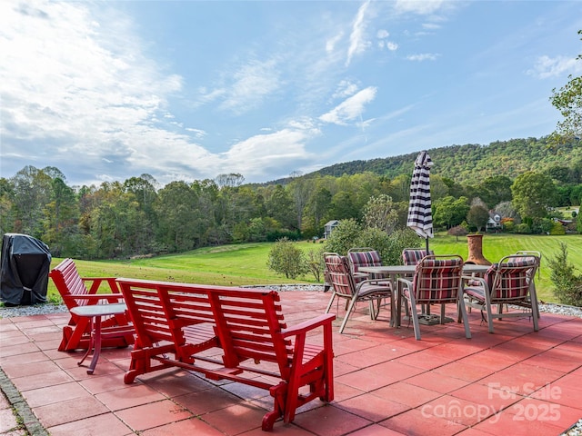 view of patio / terrace with a grill, outdoor dining area, and a view of trees