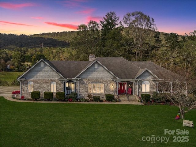 french country home featuring a chimney, a wooded view, and a yard