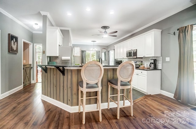 kitchen featuring a kitchen breakfast bar, white cabinetry, dark wood-type flooring, kitchen peninsula, and ornamental molding