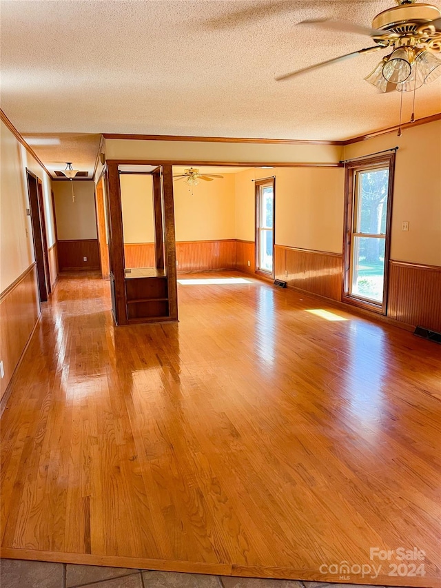 empty room featuring a textured ceiling, crown molding, ceiling fan, hardwood / wood-style flooring, and wooden walls