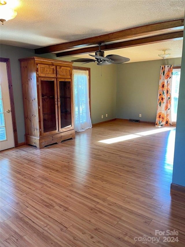 unfurnished room featuring a textured ceiling, light hardwood / wood-style floors, ceiling fan, and beamed ceiling