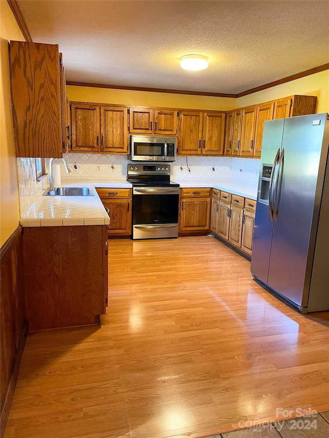 kitchen with light wood-type flooring, a textured ceiling, sink, stainless steel appliances, and crown molding