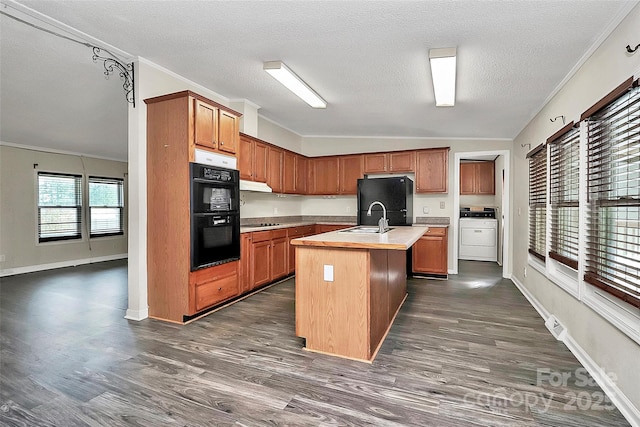 kitchen featuring ornamental molding, dark wood-type flooring, black appliances, independent washer and dryer, and an island with sink