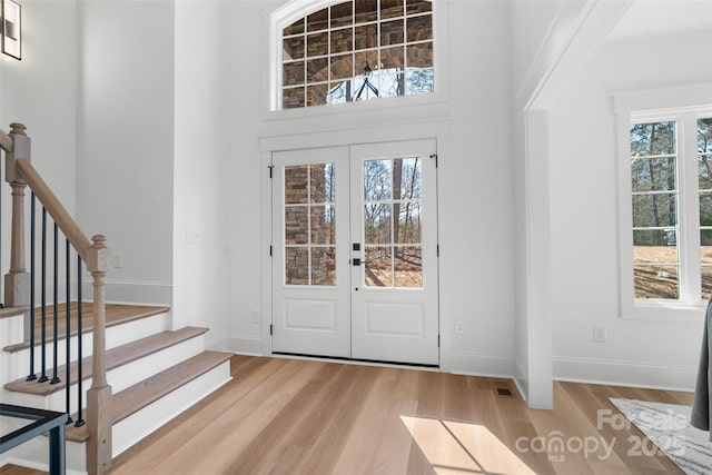 entrance foyer featuring a towering ceiling, light wood-type flooring, and french doors