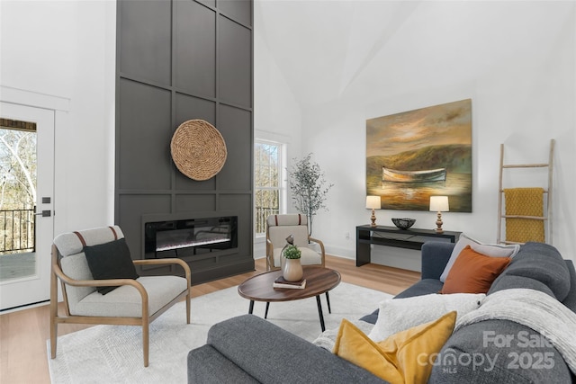 living room featuring a fireplace, high vaulted ceiling, and light wood-type flooring