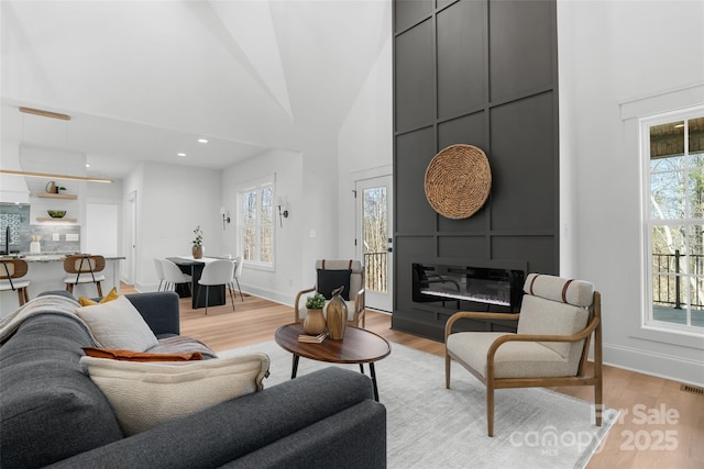 living room with a large fireplace, high vaulted ceiling, and light wood-type flooring