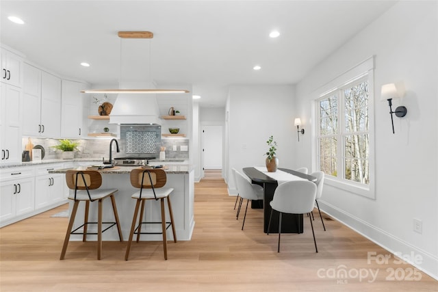 kitchen with a breakfast bar, hanging light fixtures, light stone countertops, an island with sink, and decorative backsplash