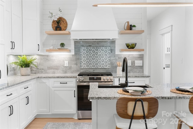 kitchen with premium range hood, a kitchen bar, light stone countertops, and stainless steel gas range oven