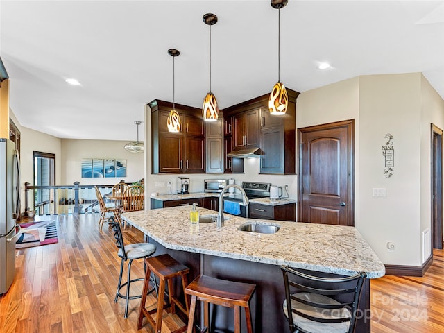 kitchen featuring appliances with stainless steel finishes, light hardwood / wood-style flooring, decorative light fixtures, a center island with sink, and sink