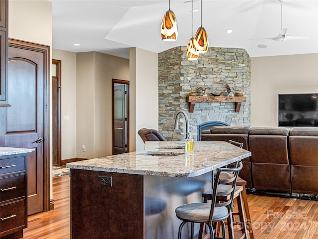 kitchen with a breakfast bar, light wood-type flooring, dark brown cabinets, ceiling fan, and a kitchen island with sink