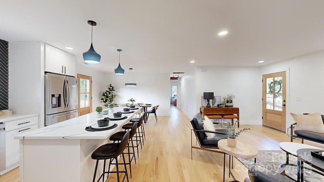 kitchen featuring stainless steel refrigerator with ice dispenser, pendant lighting, light wood-type flooring, and white cabinets