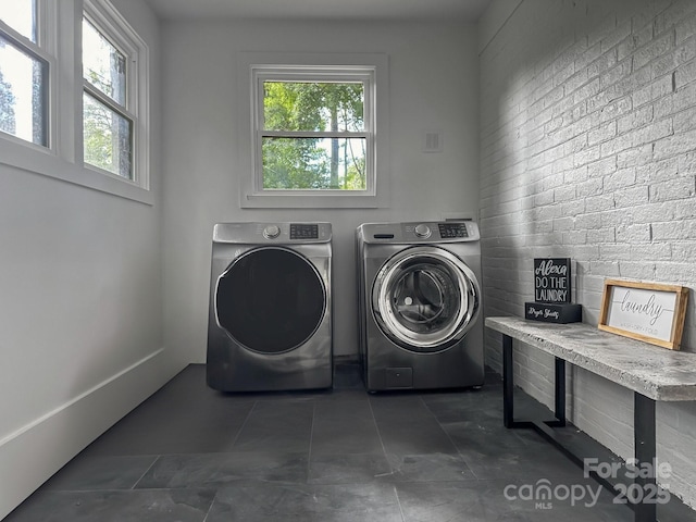 clothes washing area with washing machine and clothes dryer, brick wall, and dark tile patterned floors