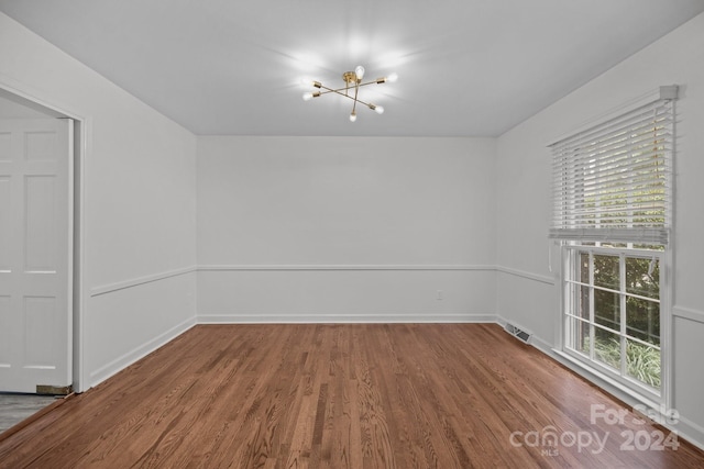 spare room featuring an inviting chandelier and hardwood / wood-style flooring