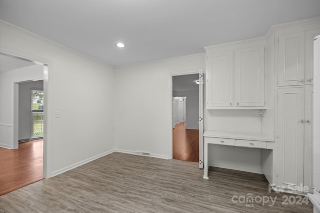 unfurnished room featuring ornamental molding, built in desk, and hardwood / wood-style flooring