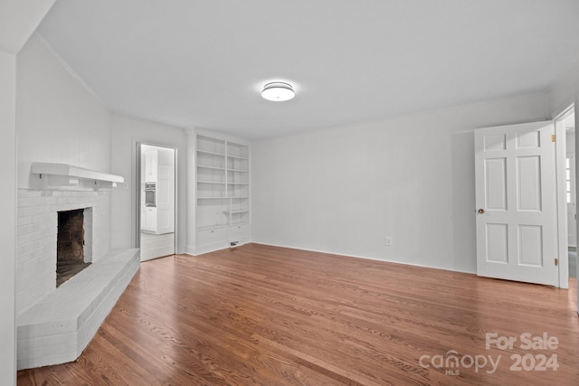 unfurnished living room with a fireplace, built in shelves, and hardwood / wood-style flooring