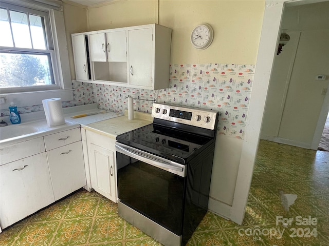 kitchen with backsplash, white cabinetry, and electric stove