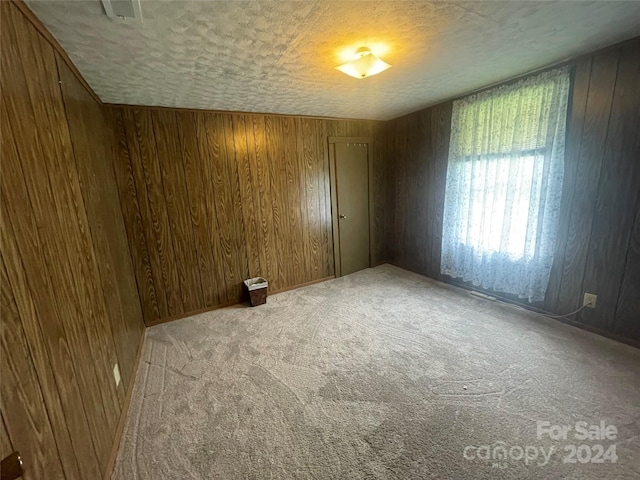 carpeted empty room with a textured ceiling and wood walls