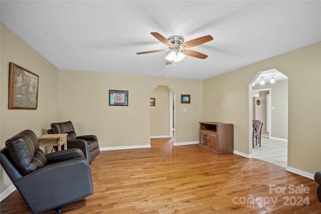 living room with ceiling fan, a textured ceiling, and light hardwood / wood-style flooring