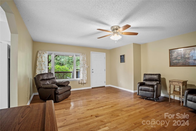 living area with ceiling fan, a textured ceiling, and light hardwood / wood-style floors