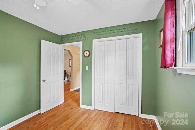 unfurnished bedroom featuring light wood-type flooring, a textured ceiling, ceiling fan, and a closet