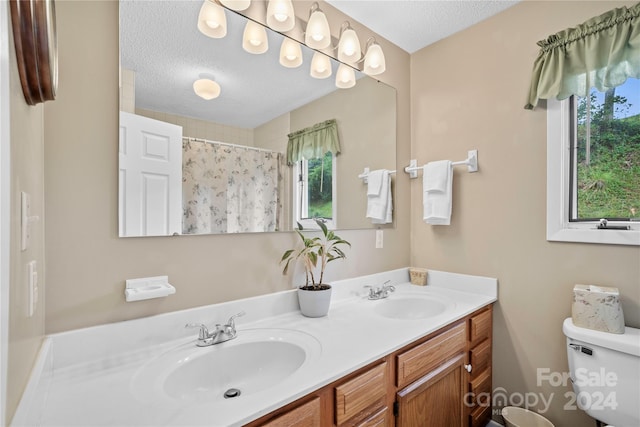 bathroom featuring vanity, toilet, a textured ceiling, and a wealth of natural light