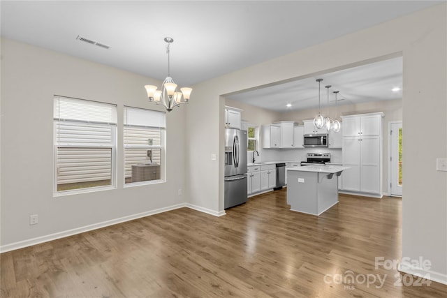 kitchen featuring appliances with stainless steel finishes, white cabinetry, a kitchen island, pendant lighting, and hardwood / wood-style floors