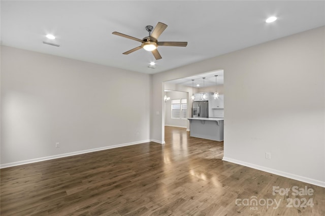 unfurnished living room featuring ceiling fan with notable chandelier and dark hardwood / wood-style flooring