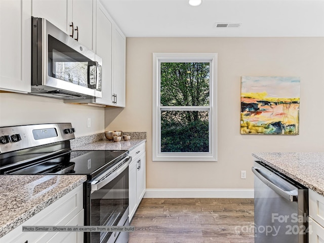 kitchen with stainless steel appliances, white cabinetry, light hardwood / wood-style floors, and light stone counters