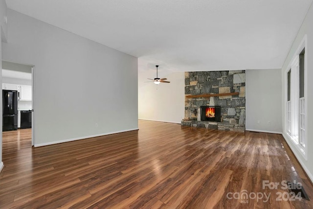 unfurnished living room featuring wood-type flooring, vaulted ceiling, ceiling fan, and a stone fireplace