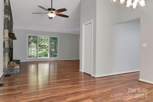 unfurnished living room with ceiling fan with notable chandelier, a fireplace, and dark wood-type flooring