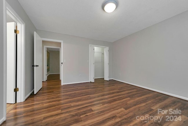 unfurnished bedroom with a spacious closet, a closet, a textured ceiling, and dark hardwood / wood-style flooring