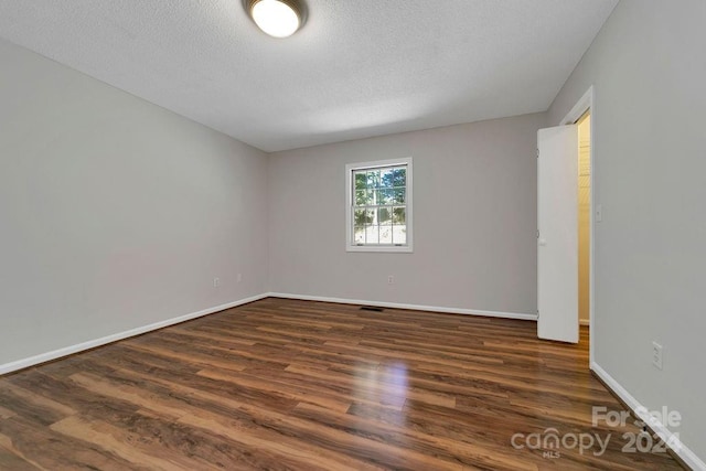 spare room featuring a textured ceiling and dark hardwood / wood-style flooring