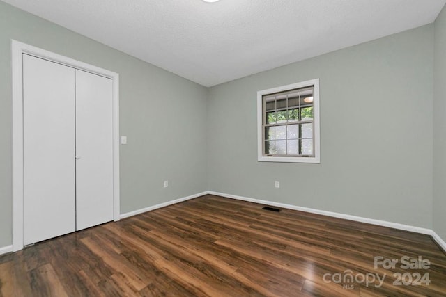 unfurnished bedroom with a closet, a textured ceiling, and dark hardwood / wood-style flooring