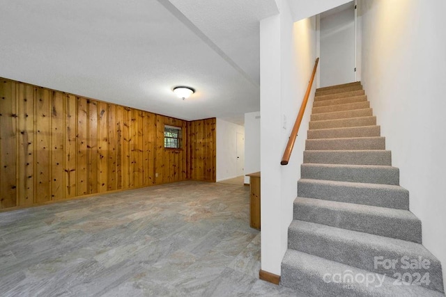 stairs featuring a textured ceiling and wooden walls