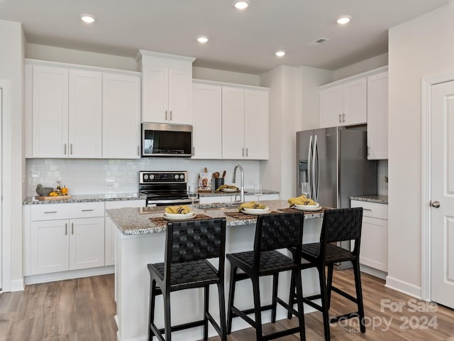 kitchen featuring a kitchen island with sink, white cabinets, appliances with stainless steel finishes, and light wood-type flooring