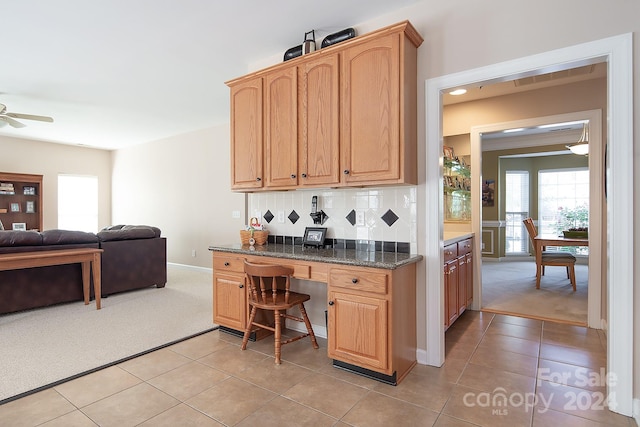 kitchen with tasteful backsplash, built in desk, light carpet, ceiling fan, and dark stone counters