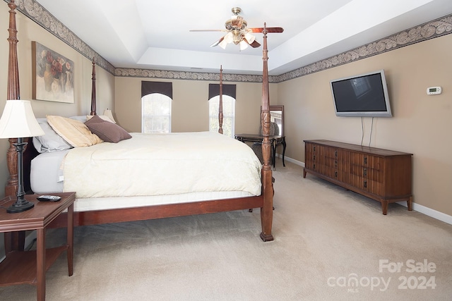 bedroom featuring ceiling fan, a raised ceiling, and light carpet